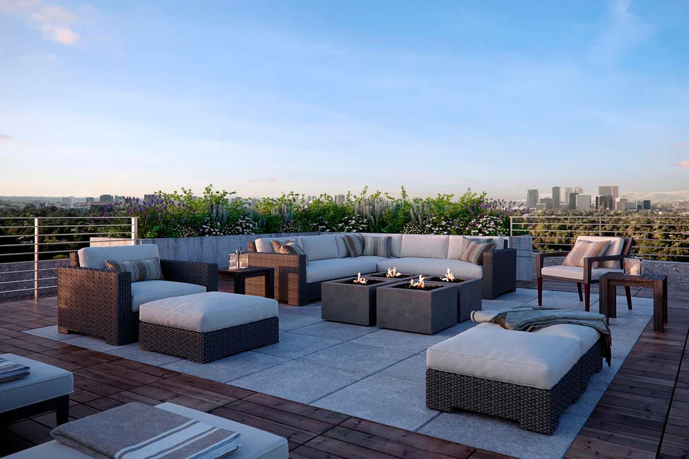 Luxury rooftop patio with two square gas fire pits, surrounded by white cushioned lounge seating and palm trees at sunset