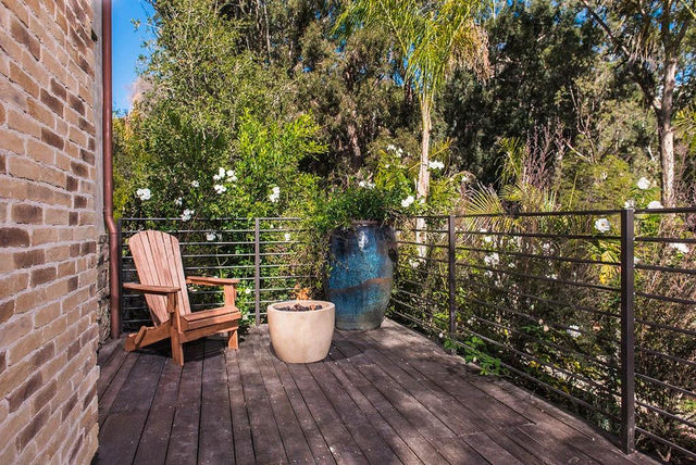 Cozy wood deck with a small round gas fire bowl, Adirondack chair, and lush garden view
