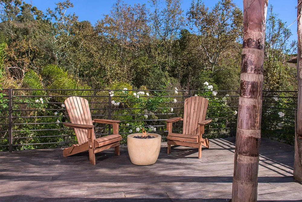 Cozy wood deck with a small round gas fire bowl, Adirondack chair, and lush garden view