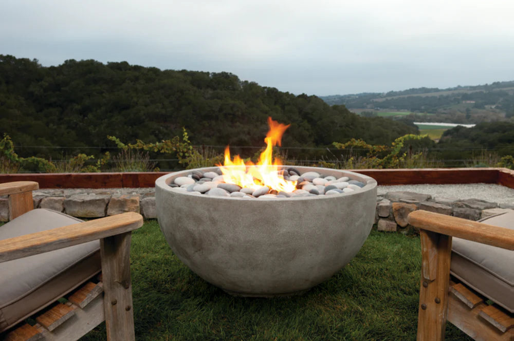 An outdoor gas fire pit named 'Infinite' with a Travertine finish, surrounded by seating areas, with a scenic landscape in the background.