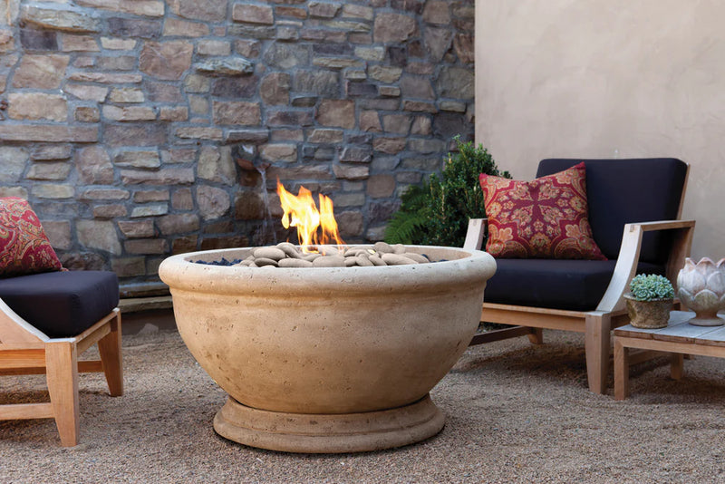 Garden seating area surrounded by stone wall with a lit gas burning fire pit and stylish modern outdoor furniture.