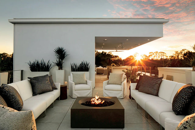 Modern rooftop fire pit with a square propane fire pit surrounded by white outdoor sofas at sunset